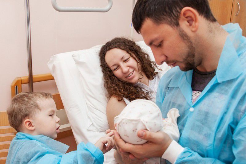 Photograph of a father, mother and young boy looking at a newborn baby in a hospital.