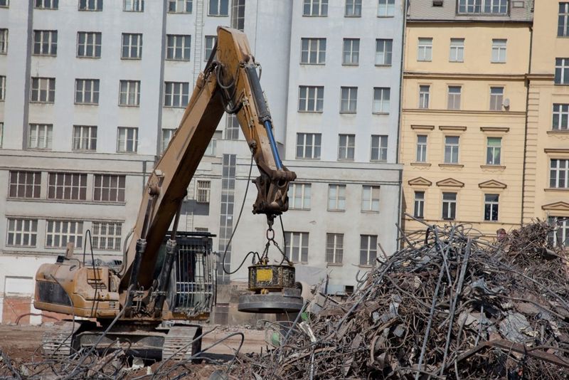 Photograph of a digger equipped with a magnet lifting heavy construction debris in a city.