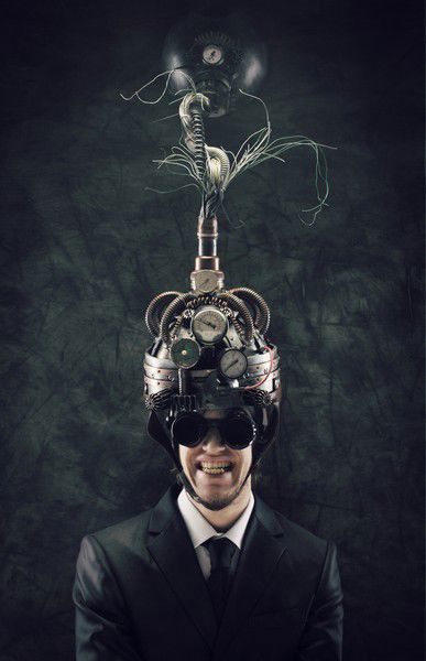 A photograph showing a young man in a suit wearing a strange metal device and glasses on his head.