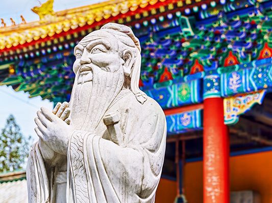 A photograph showing a statue of a bearded man in front of a Chinese temple.