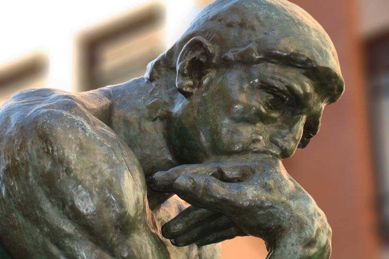 A photograph of Rodin's The Thinker, a famous statue of a man sitting and leaning his head on his hand in deep thought.