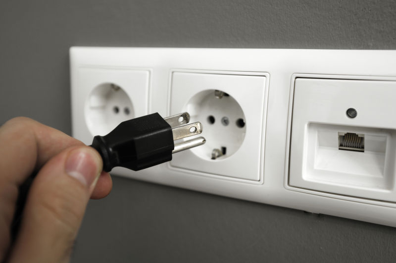 Photograph of a person plugging a power cord into a wall socket.
