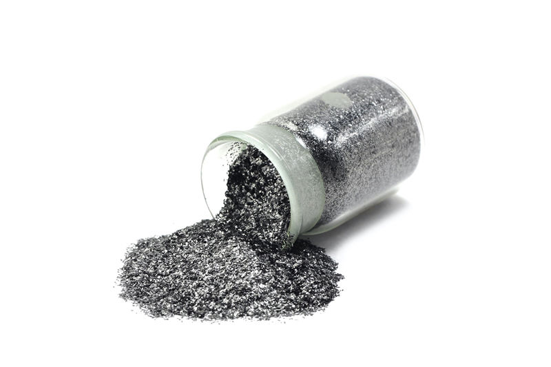 Photograph of graphite powder spilling from a glass container on white background