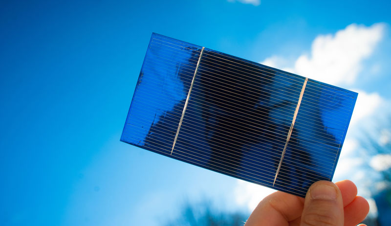 Photograph of a person holding a small solar cell in his hand.