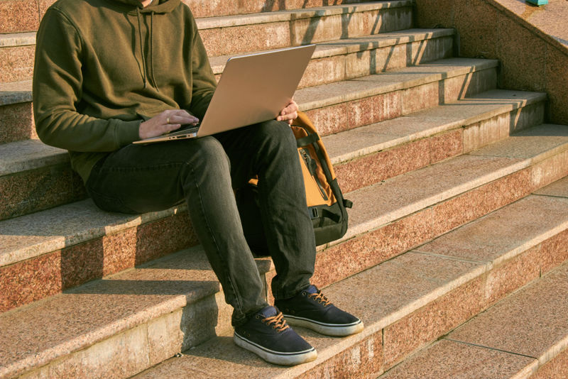 A young man sitting on steps with a laptop.