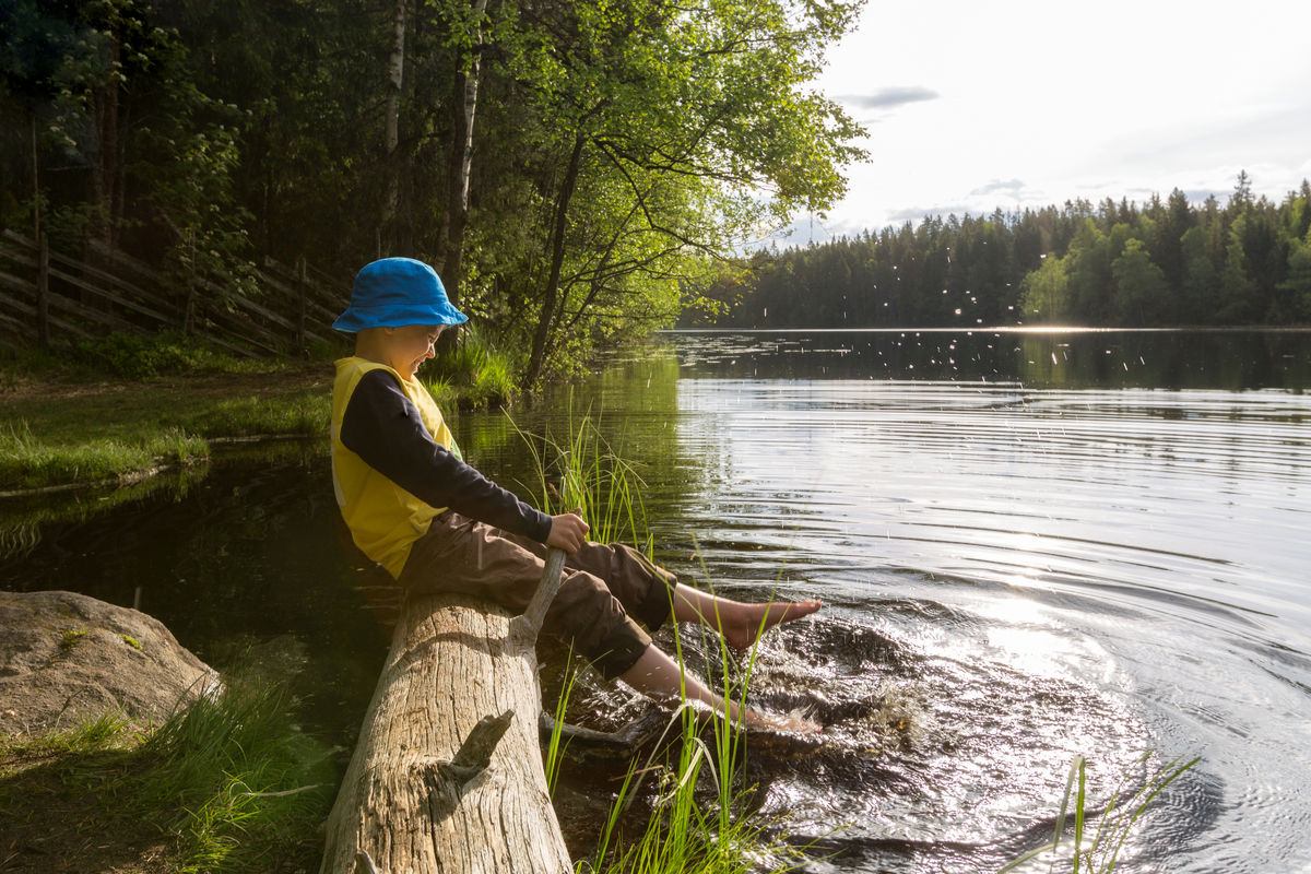 Photograph of a boy bathing his feet in a lake during the summer.